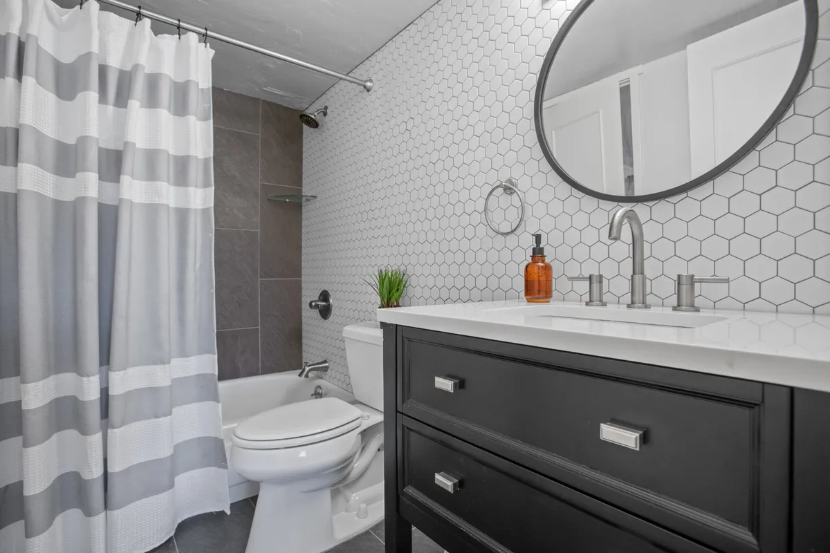 A modern bathroom interior is presented, featuring a hexagonal tile accent wall, a round mirror above a contemporary sink, and a fresh, inviting mood ideal for personal care routines or unwinding after a long day.