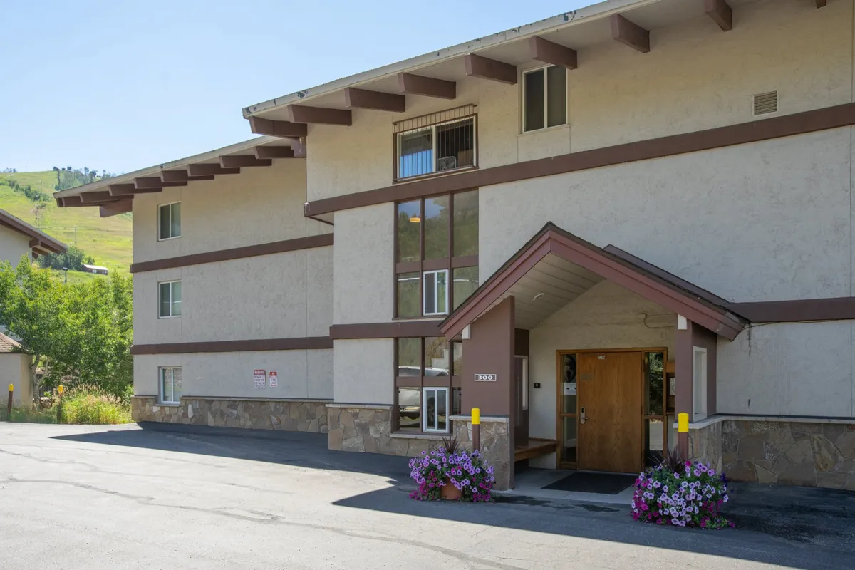 A welcoming view of the building’s main entrance, adorned with seasonal flower arrangements and inviting landscaping. The facade hints at a recently renovated, well-kept property, supporting the sanctuary theme.