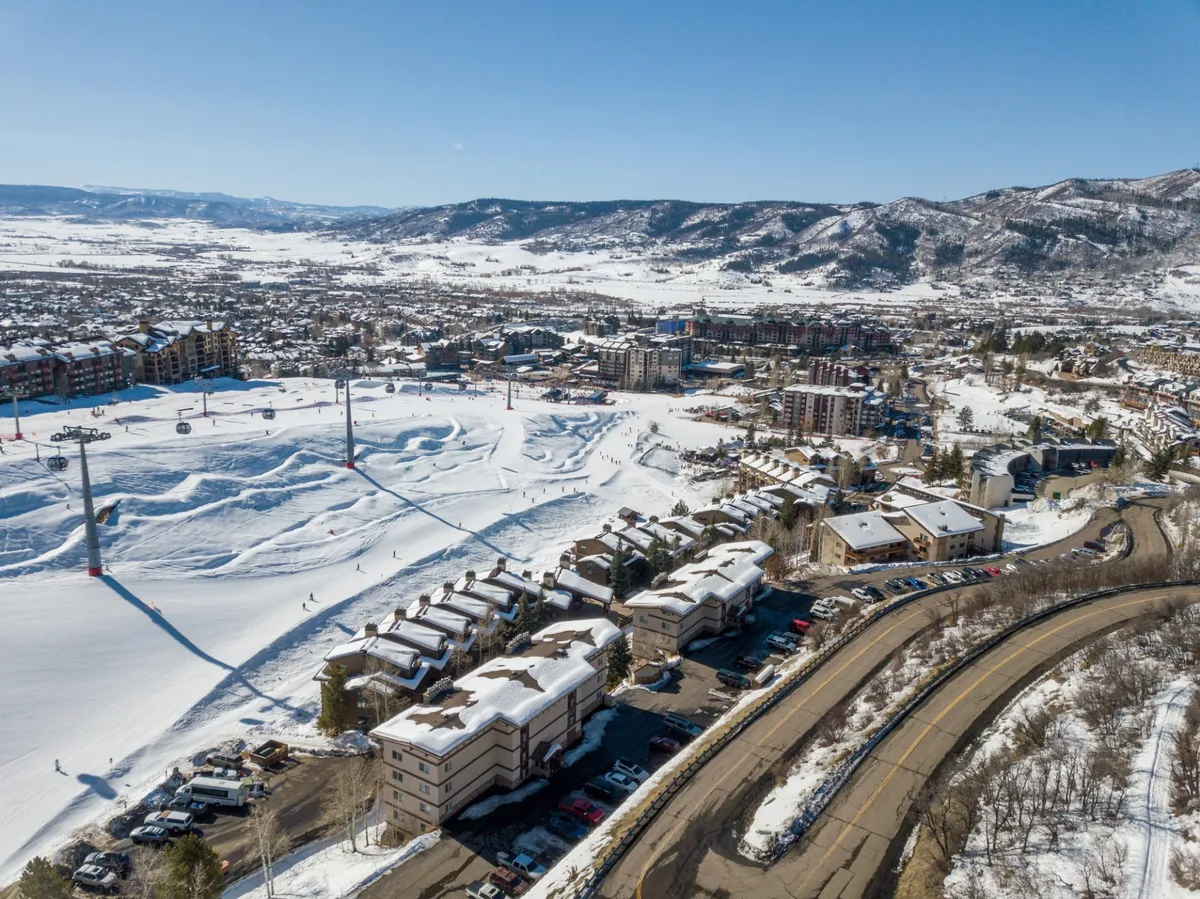 A wide view of the snow-covered ski slopes with ski lifts, residential buildings, and the mountain range in the background. The image conveys the thrill of winter sports with a cozy, inviting vibe—perfect for showcasing sunset views after an active day outdoors.