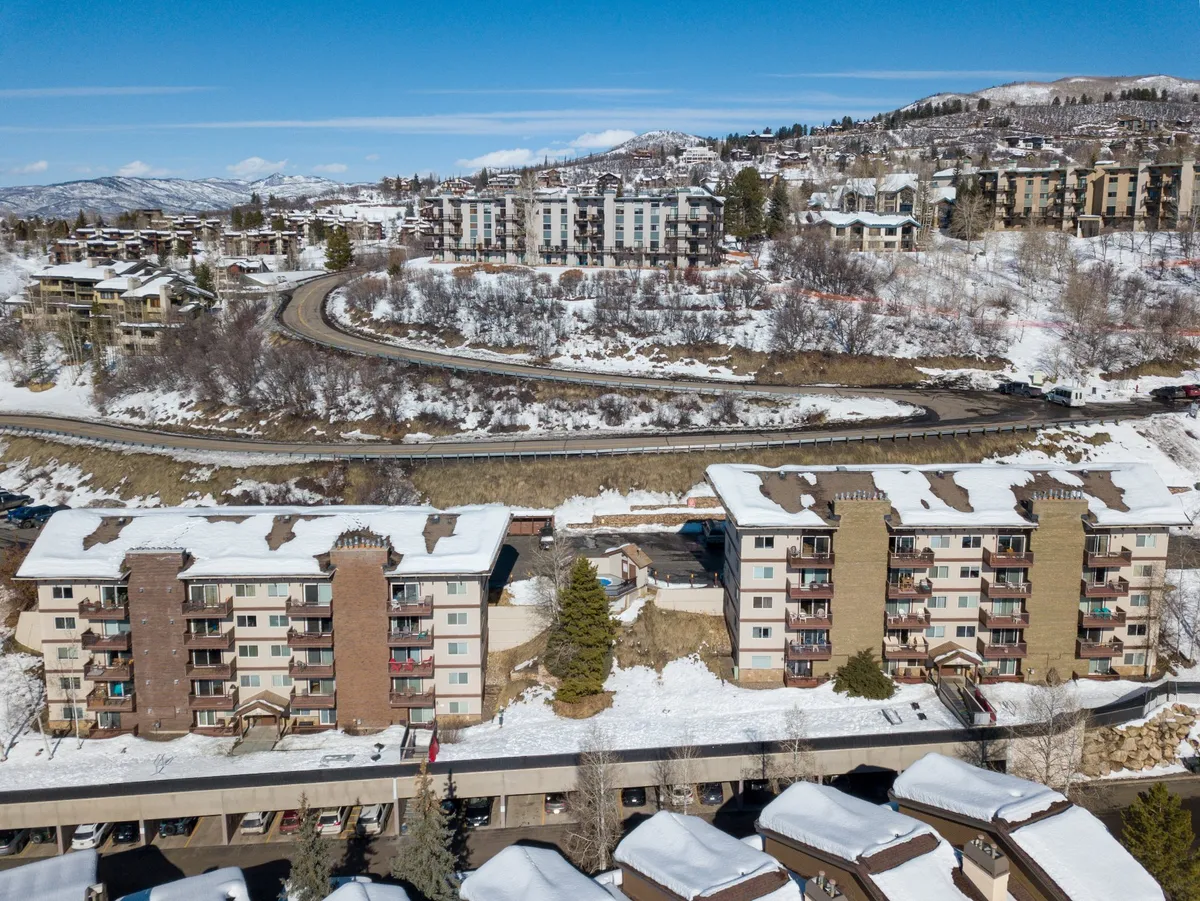 A serene exterior shot with snow-capped buildings nestled along a winding road, set against a dramatic mountain backdrop. The tranquil ambiance is complemented by wintery scenery, inviting thoughts of cozy evenings and adventurous days in nature.