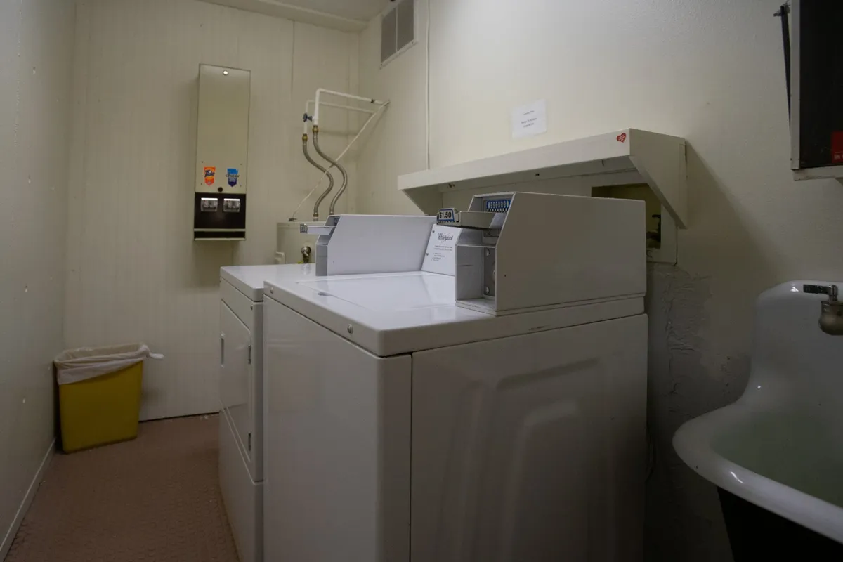 A communal laundry room equipped with several washing machines and dryers, a countertop with a sink, and a large mirror. The space is clean, functional, and designed for shared use, making longer stays more comfortable for guests.