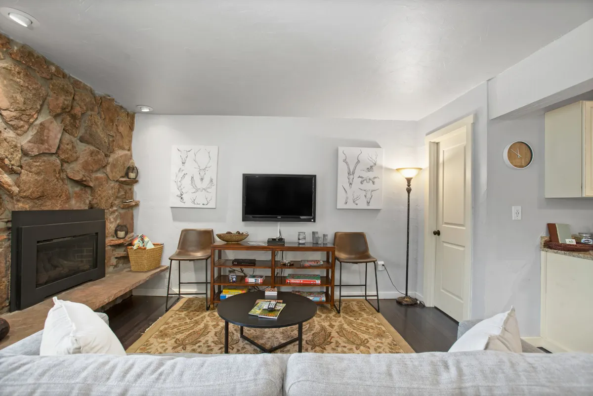 A cozy living room with a stone fireplace, flatscreen TV, coffee table, armchairs, and tasteful artwork. The arrangement is ideal for relaxing, movie nights, or board games, and the space feels inviting and conducive to family gatherings.