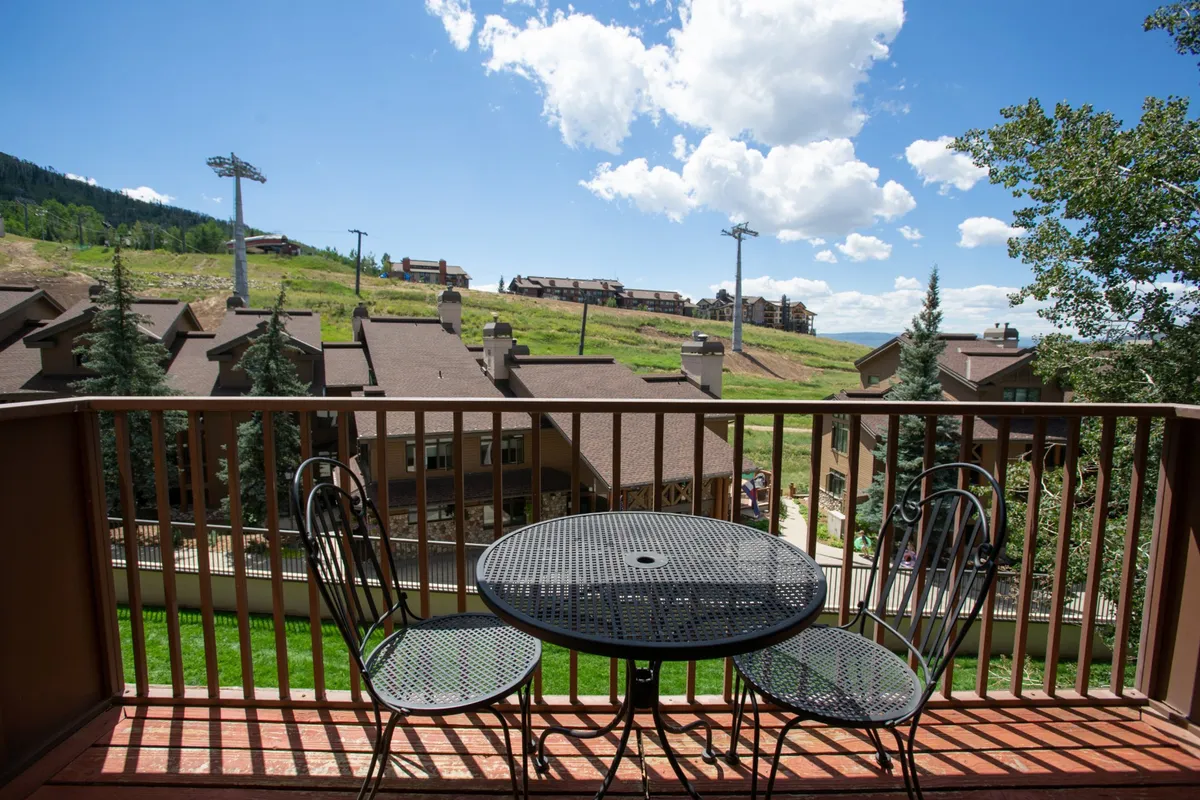 A serene balcony with a table and chairs overlooks a sweeping mountain landscape, providing an inviting spot for coffee, reading, or simply enjoying the view.