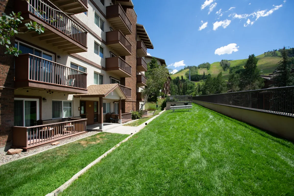 Serene balconies and a green lawn frame a mountain view, illustrating the relaxing transition from adventure to leisure. The scene hints at residents enjoying coffee outdoors or unwinding after a day on the trails.