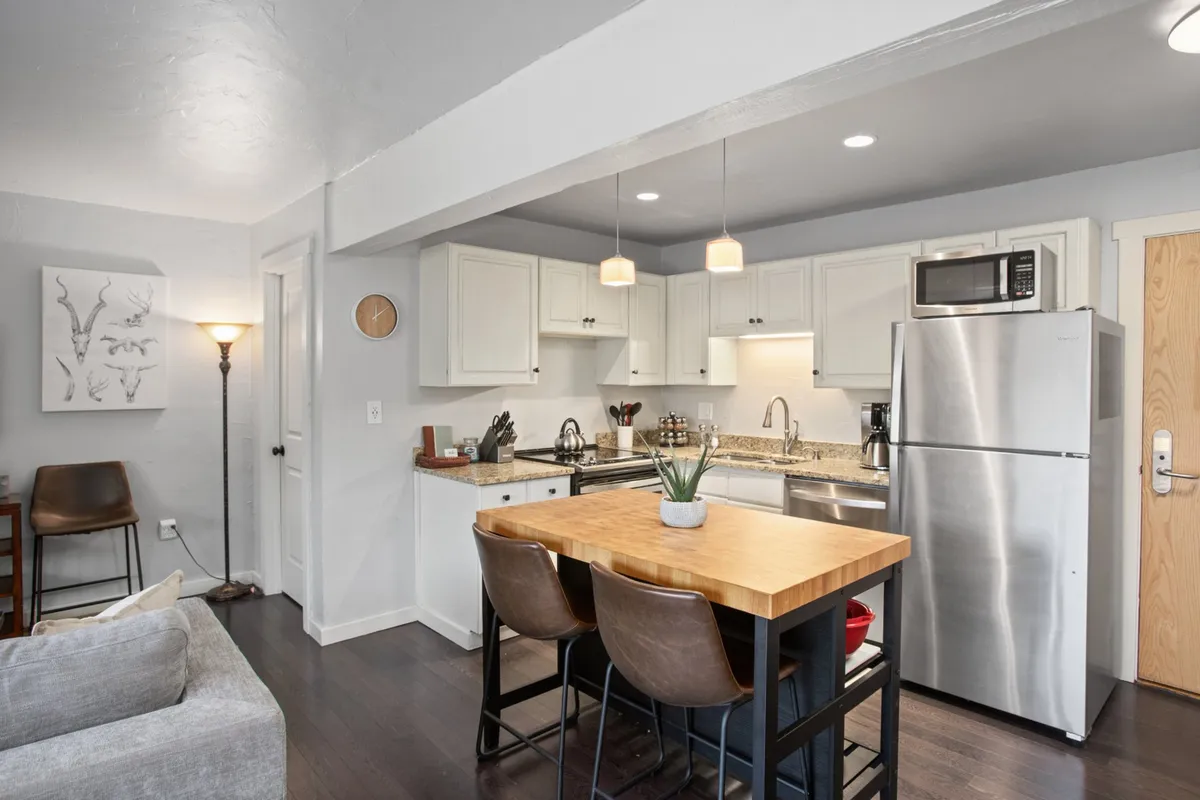 A warmly lit kitchen space featuring a central kitchen island with bar stools, stainless steel appliances, modern light fixtures, and tasteful wall art. The setting is inviting, with the island serving as both a prep and dining space, and the appliances reflecting a recent renovation. The overall ambiance is cozy and perfect for social gatherings or family cooking sessions.