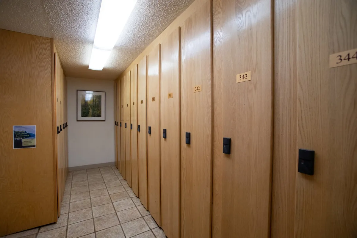 A tidy, modern interior space lined with secure storage lockers, illuminated by warm lighting and accented with tasteful wall art. The hallway feels organized and functional, highlighting the practical amenity of ski lockers for guests’ gear storage.